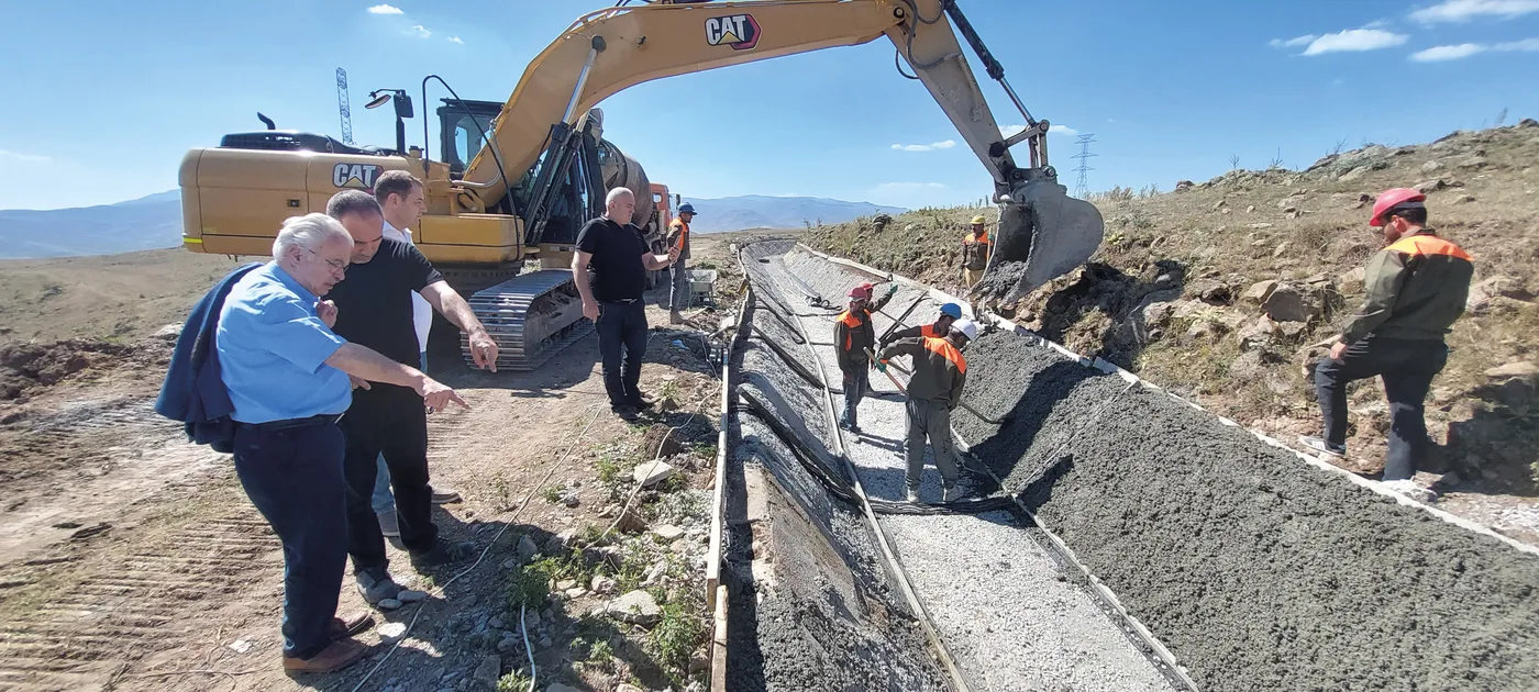 Pelleteuse et ouvriers bétonnant le lit du canal de Spandaryan, observés par des visiteurs sur le chantier